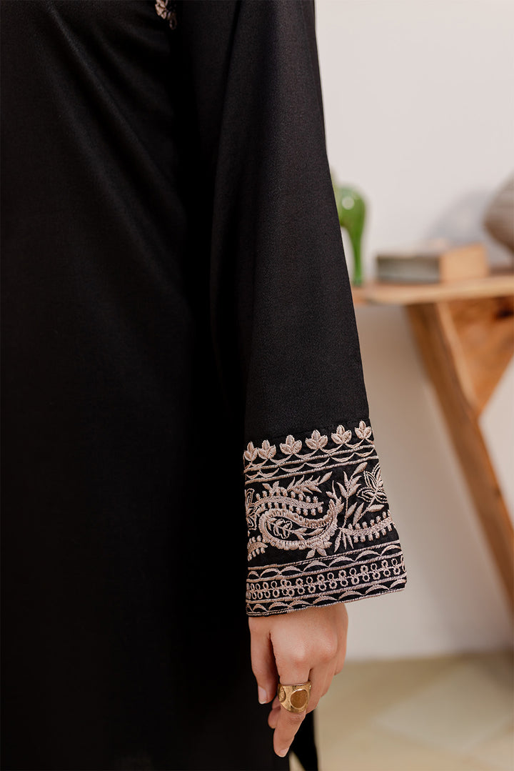 Close-up of a black embroidered garment sleeve with floral design and a hand wearing a ring.