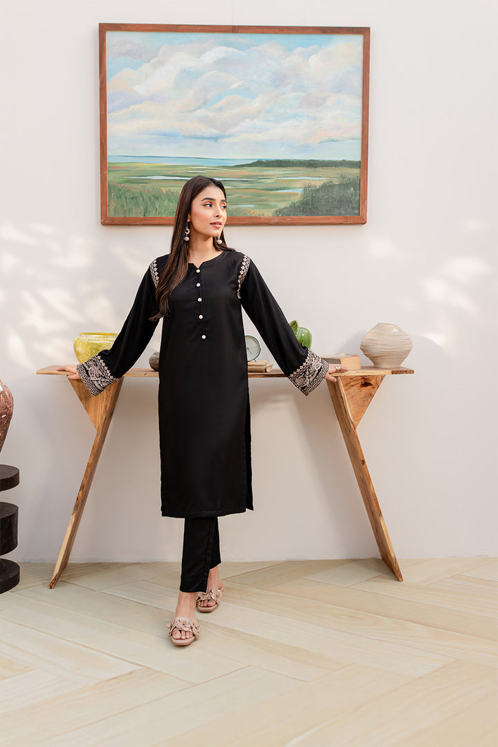 Woman in black cotton slub 2PC fashion wear with decorative sleeves, standing beside a stylish table.