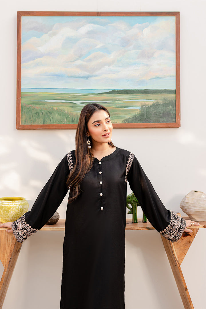 Woman in a black embroidered outfit standing in a decorated indoor space.