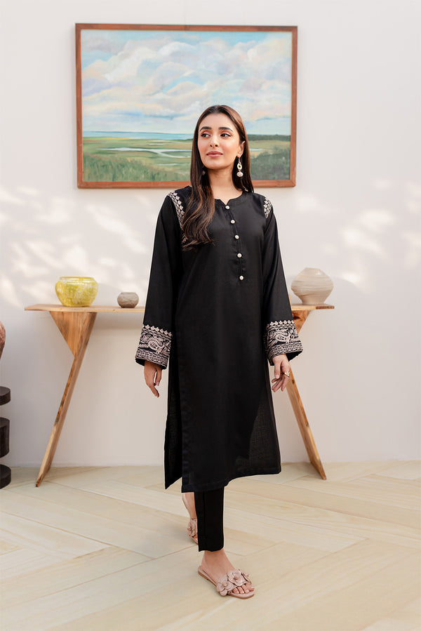 A woman in a black 2PC outfit with embroidered sleeves, standing in a stylishly decorated room.